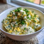A close-up of a white bowl filled with chunky Keto Creamy Herb Deviled Egg Salad, topped with fresh chives and dill.