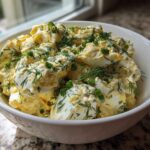 A white bowl filled with Keto Creamy Herb Deviled Egg Salad, topped generously with fresh dill and chopped green onions.