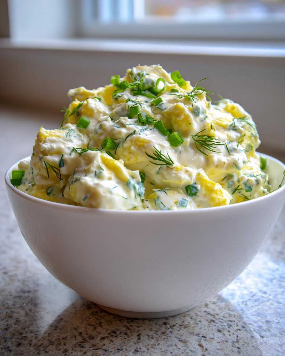 A white bowl filled high with Keto Creamy Herb Deviled Egg Salad, topped with fresh green onions and dill.