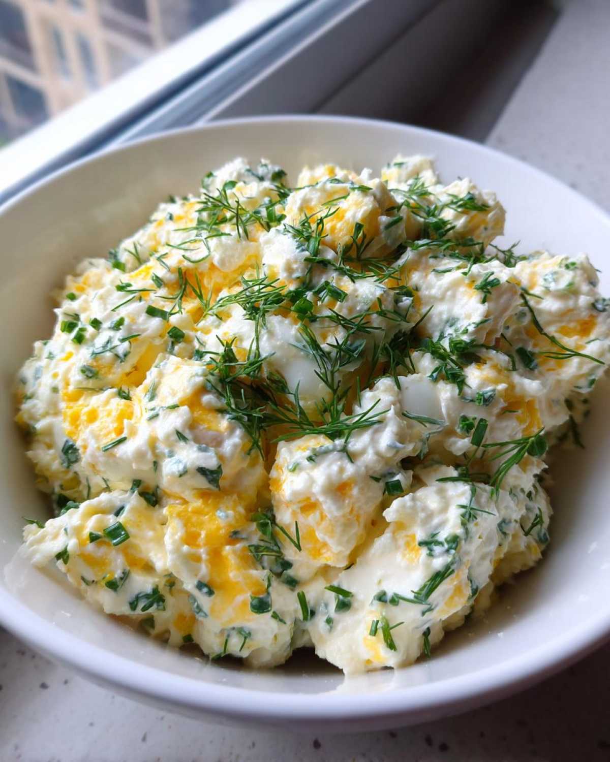 Close-up of a white bowl filled with Keto Creamy Herb Deviled Egg Salad, topped with fresh dill and chives.