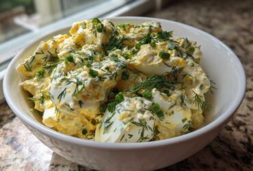 A white bowl filled with Keto Creamy Herb Deviled Egg Salad, topped generously with fresh dill and chopped green onions.