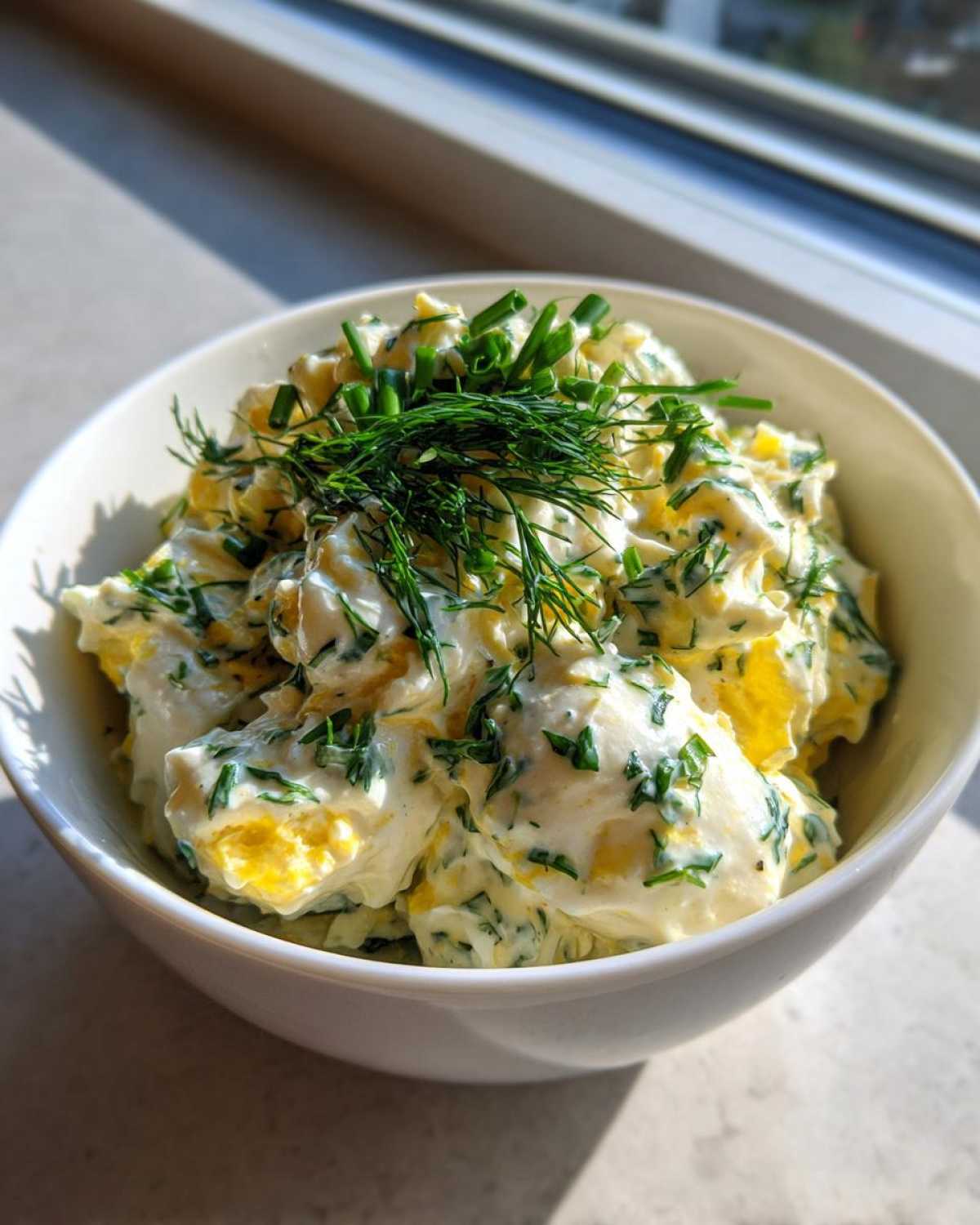 A white bowl filled with Keto Creamy Herb Deviled Egg Salad, topped generously with fresh dill and chives.