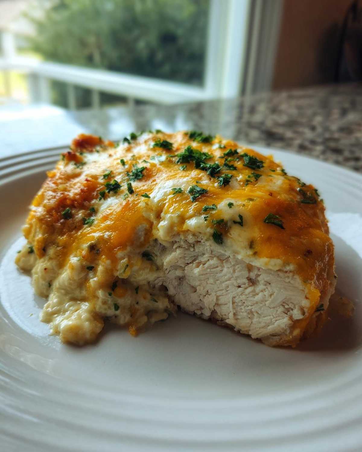 A cross-section view of Keto Creamy Jalapeno Popper Chicken, showing juicy white meat topped with melted cheese and herbs.
