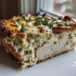 A cross-section of Keto Creamy Jalapeno Popper Chicken showing juicy white meat topped with melted cheese and green herbs.