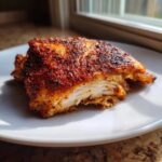 Cross-section of Keto Crispy Baked Chicken Thighs showing moist white meat and a heavily seasoned, crispy, reddish-brown exterior.