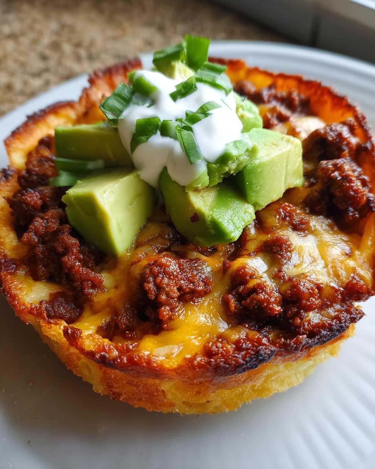 Close-up of a Keto Crispy Cheese Taco Shell Bowl filled with seasoned ground meat, melted cheese, avocado, sour cream, and green onions.