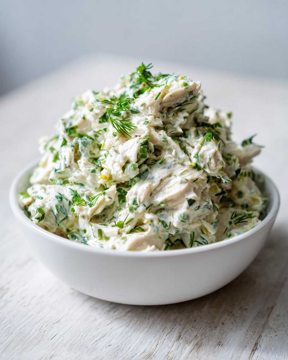 A generous serving of creamy Keto Lemon Herb Chicken Salad, mixed with fresh green herbs, piled high in a white bowl.