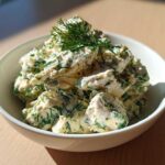 A white bowl filled with creamy Keto Lemon Herb Chicken Salad, heavily mixed with green herbs like dill.