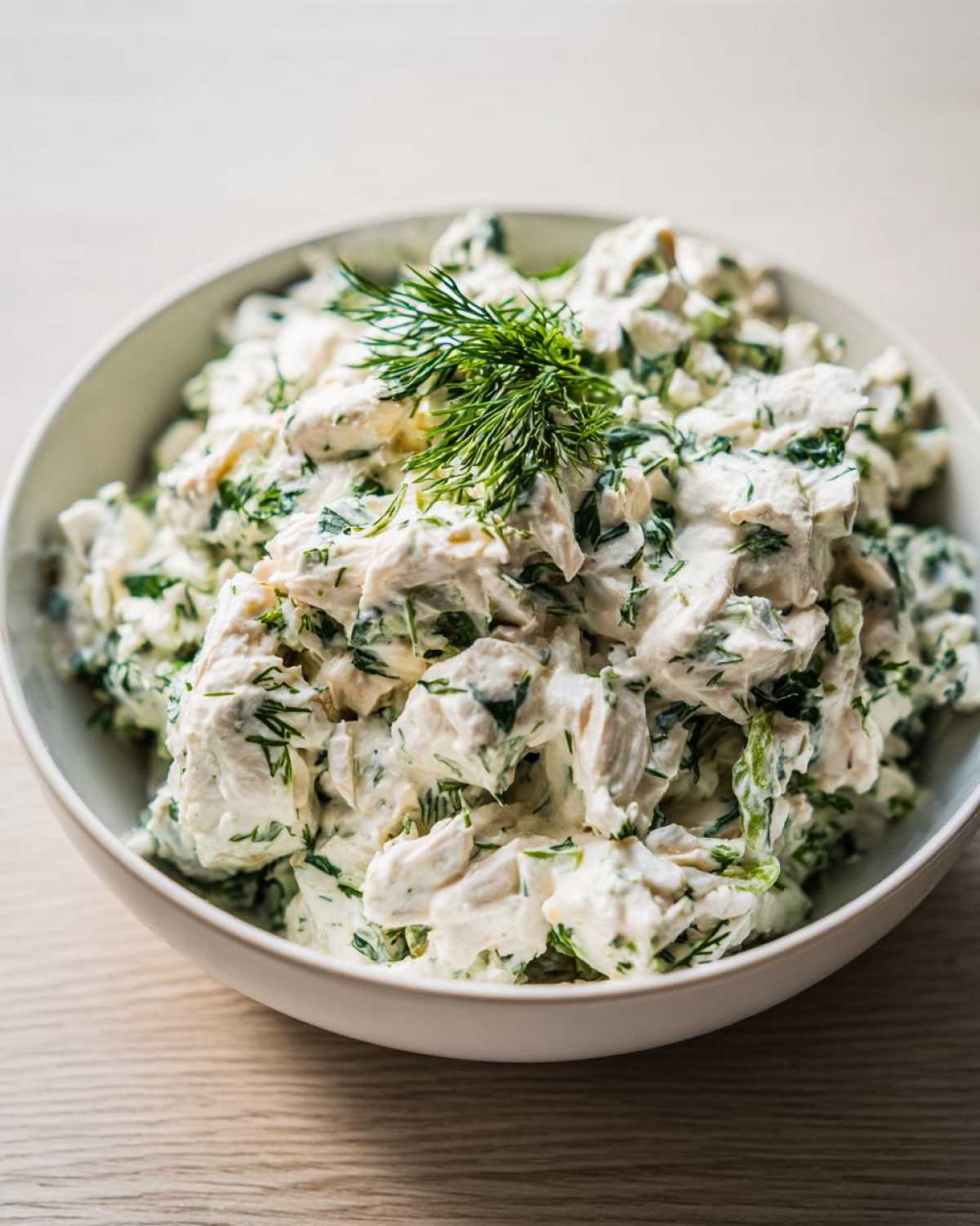 A white bowl filled with creamy Keto Lemon Herb Chicken Salad, garnished with fresh dill.