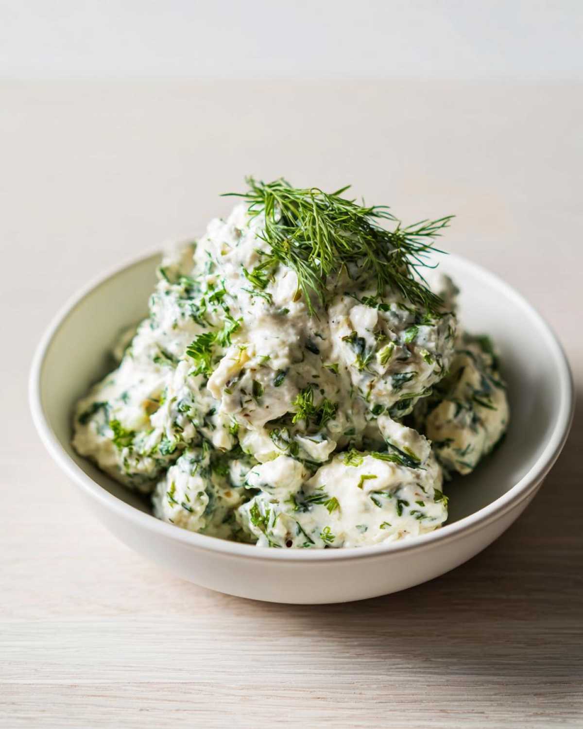 A white bowl filled with creamy Keto Lemon Herb Chicken Salad generously mixed with green herbs and topped with fresh dill.