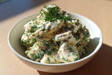 A white bowl filled with creamy Keto Lemon Herb Chicken Salad, heavily mixed with green herbs like dill.