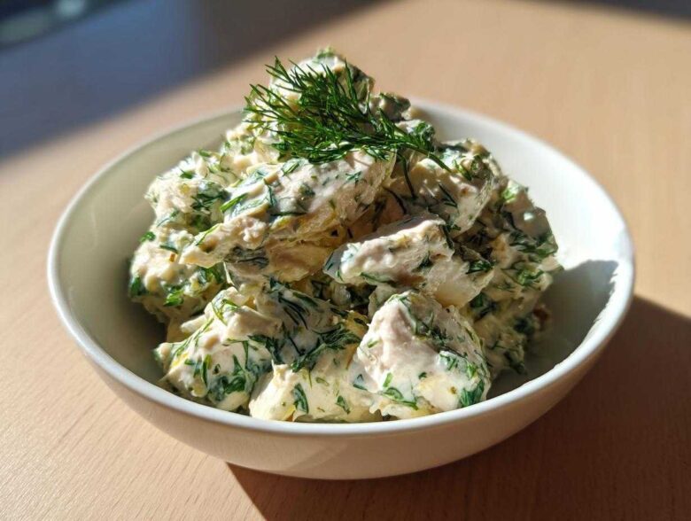 A white bowl filled with creamy Keto Lemon Herb Chicken Salad, heavily mixed with green herbs like dill.