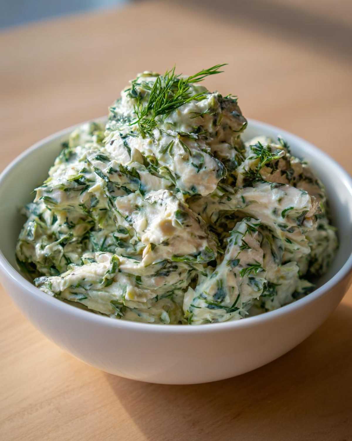 A close-up of creamy Keto Lemon Herb Chicken Salad mixed with green herbs, served in a white bowl.