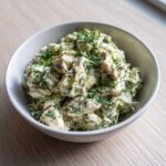 Close-up of a white bowl filled with Keto Lemon Herb Chicken Salad, generously topped with fresh dill.