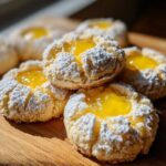 A close-up stack of bright Lemon Lavender Thumbprint Cookies dusted heavily with powdered sugar and filled with vibrant yellow lemon curd.