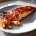 Close-up of a flaky, glazed fillet of Maple Dijon Glazed Baked Salmon on a white plate.