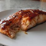 Close-up of a perfectly cooked Maple Dijon Glazed Baked Salmon fillet flaking apart on a white plate.