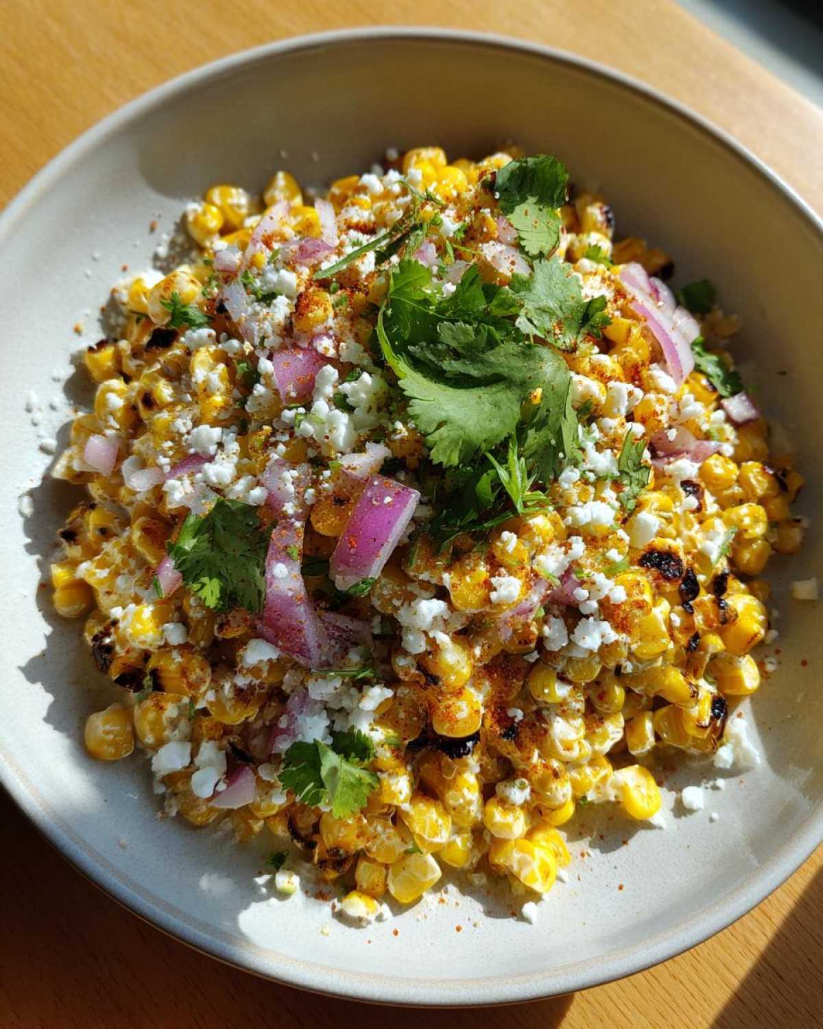 Close-up of a bowl filled with vibrant Mexican street corn salad featuring charred corn, cotija cheese, red onion, and fresh cilantro.