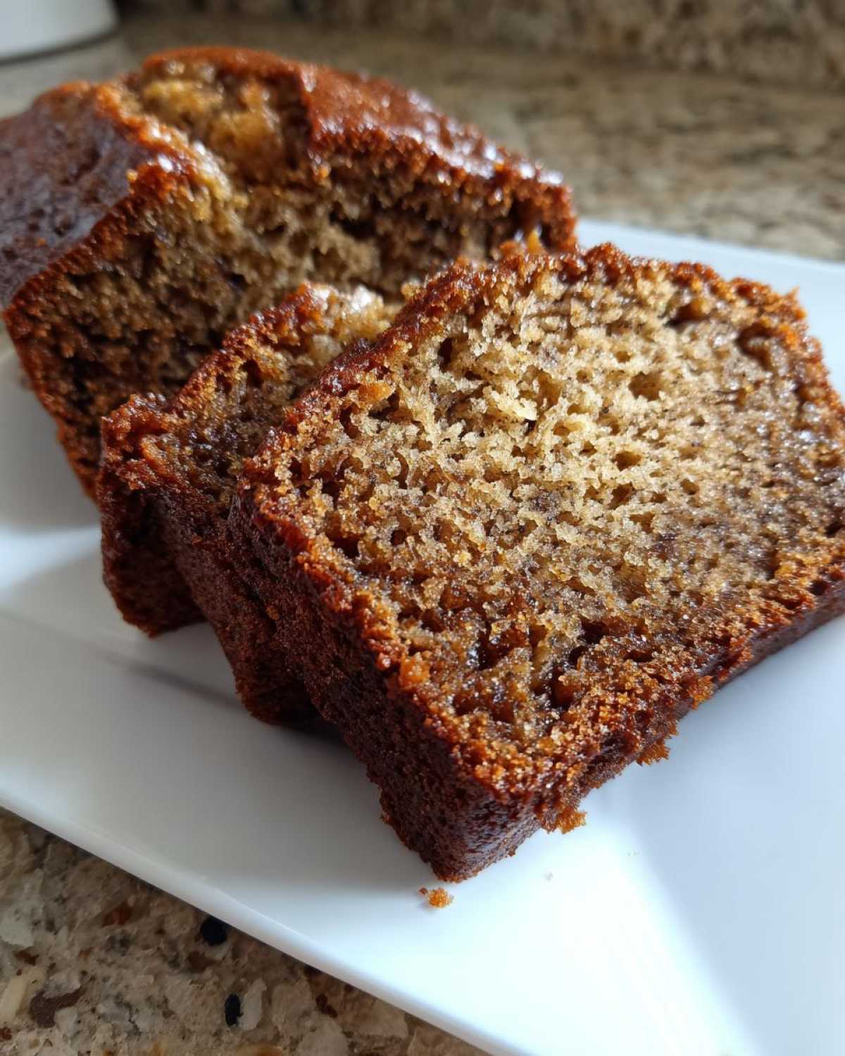 Close-up of moist, dark brown slices of banana bread displayed on a white plate, showing the texture from The Banana Bread Step by Step.