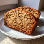 Two thick, moist slices of freshly baked banana bread resting on a white plate, showcasing the crumb texture.