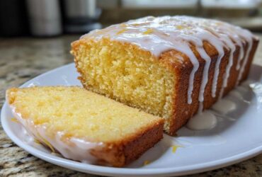 A moist Lemon Loaf cake, partially sliced, covered in a thick white lemon glaze and zest.