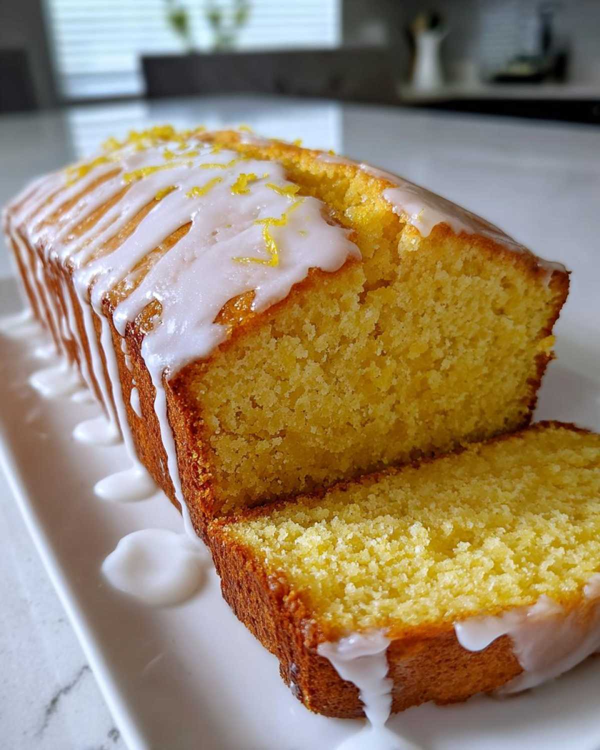 Close-up of a moist Lemon Loaf cake, sliced, topped with white glaze and bright yellow lemon zest.