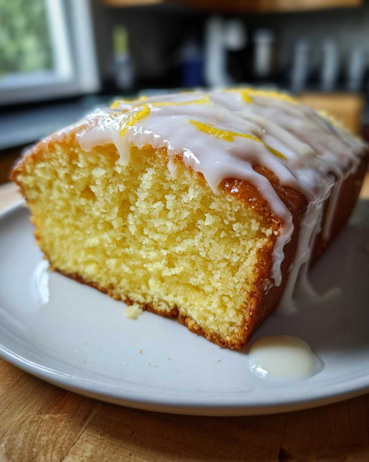 Close-up of a moist slice of Lemon Loaf cake topped with thick white glaze and lemon zest.