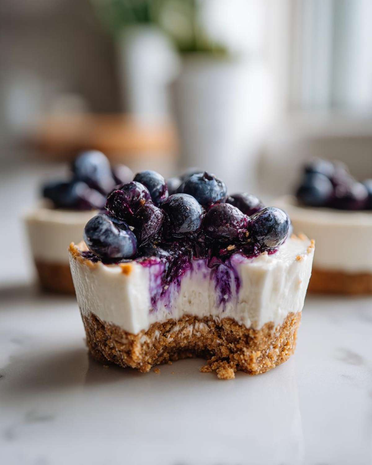 Close-up of a No-Bake Blueberry Cheesecake Oat Cup with a bite taken out, showing the crust and creamy filling topped with fresh blueberries.