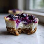 Close-up of a No-Bake Blueberry Cheesecake Oat Cup with a bite taken out, showing the creamy filling and oat crust.