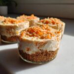 Four individual No-Bake Carrot Cake Cheesecake Cups with graham cracker crusts and shredded carrot topping.