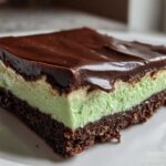 A close-up of a layered No-Bake Chocolate Mint Icebox Bars slice with a chocolate crust, mint filling, and chocolate ganache topping.