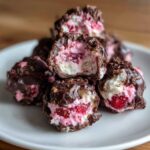 Close-up of No-Bake Chocolate Strawberry Yogurt Clusters stacked, showing the creamy white and pink yogurt filling with strawberry pieces inside the dark chocolate shell.