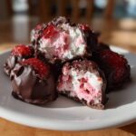 A pile of No-Bake Chocolate Strawberry Yogurt Clusters, partially dipped in chocolate, with one cluster broken open showing the pink and white yogurt filling.