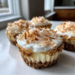 Four individual No-Bake Lemon Coconut Cheesecake Cups topped with whipped cream and toasted coconut flakes.