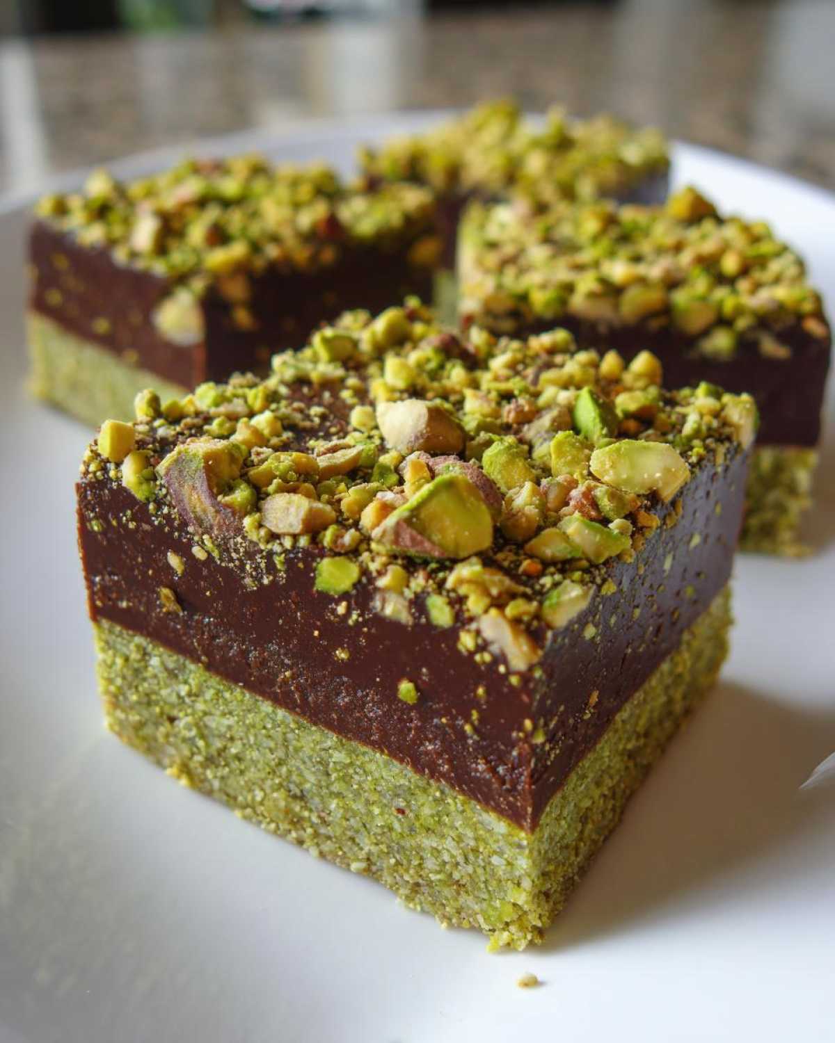 Close-up of a square piece of No-Bake Pistachio Chocolate Fudge Squares with a green pistachio layer and chocolate top.
