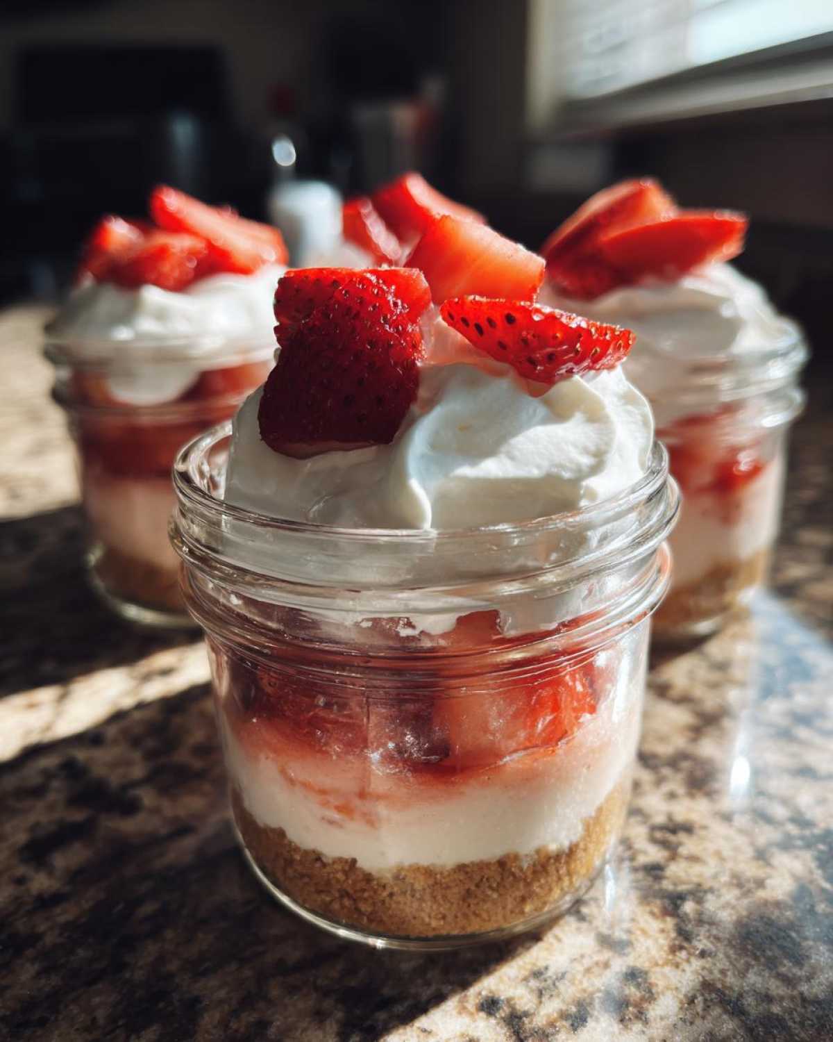 Close-up of layered No-Bake Strawberry Cream Pie Jars topped with whipped cream and fresh strawberry slices.