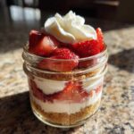Close-up of a No-Bake Strawberry Cream Pie Jars layered with graham cracker crust, cream filling, and fresh strawberries, topped with whipped cream.