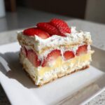 A perfect slice of No-Bake Strawberry Lemon Icebox Cake showing layers of cream, lemon filling, and fresh strawberries.
