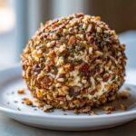 A close-up of a perfectly formed cheese ball recipe coated entirely in chopped nuts and herbs.