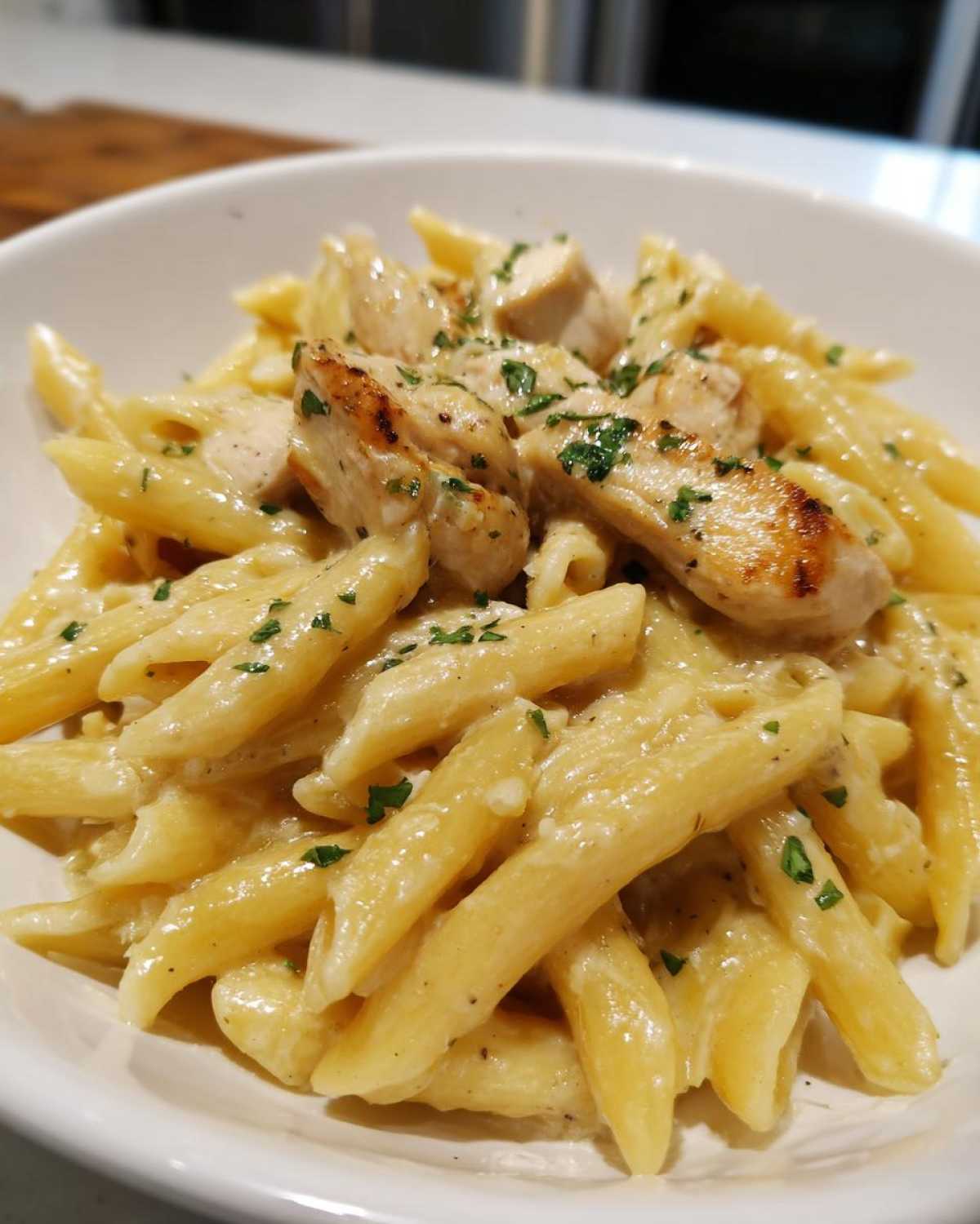 Close-up of creamy chicken pasta featuring penne noodles, grilled chicken pieces, and parsley garnish.