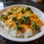 A close-up of a white bowl filled with fluffy white rice topped generously with bright green broccoli florets covered in a rich, orange One-Pot Creamy Broccoli Cheddar Rice sauce.