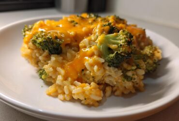 Close-up of a serving of One-Pot Creamy Broccoli Cheddar Rice topped with melted cheddar cheese and visible broccoli florets.