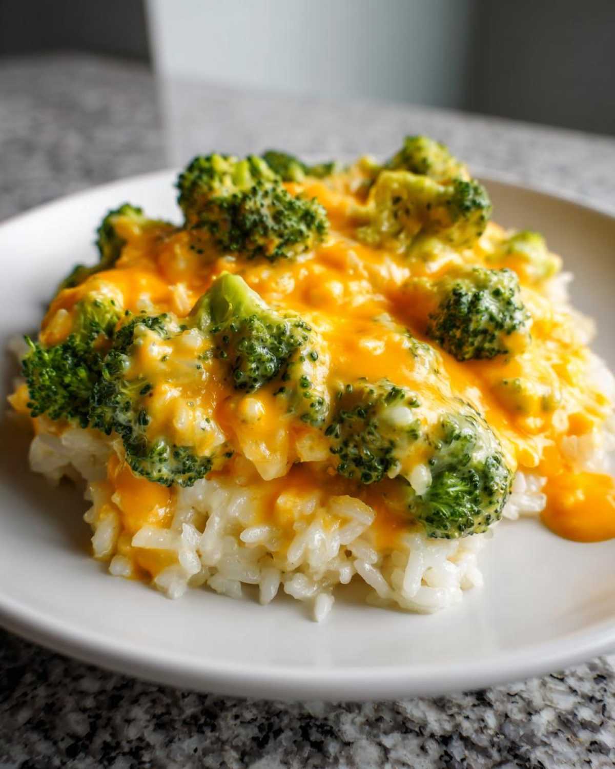 Close-up of a serving of One-Pot Creamy Broccoli Cheddar Rice topped with melted cheddar cheese and bright green broccoli florets.