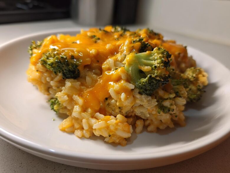 Close-up of a serving of One-Pot Creamy Broccoli Cheddar Rice topped with melted cheddar cheese and visible broccoli florets.