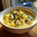 Close-up of a white bowl filled with One-Pot Creamy Lemon Chicken Noodle Soup, topped with parsley.