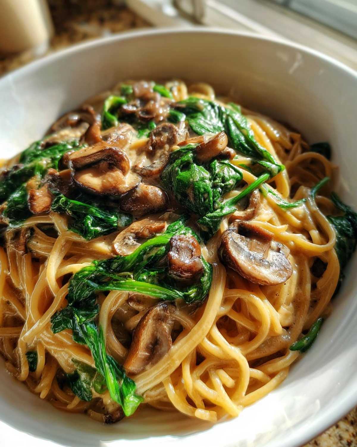 Close-up of One-Pot Creamy Mushroom Spinach Ramen noodles coated in a rich sauce with sautéed mushrooms and wilted spinach.