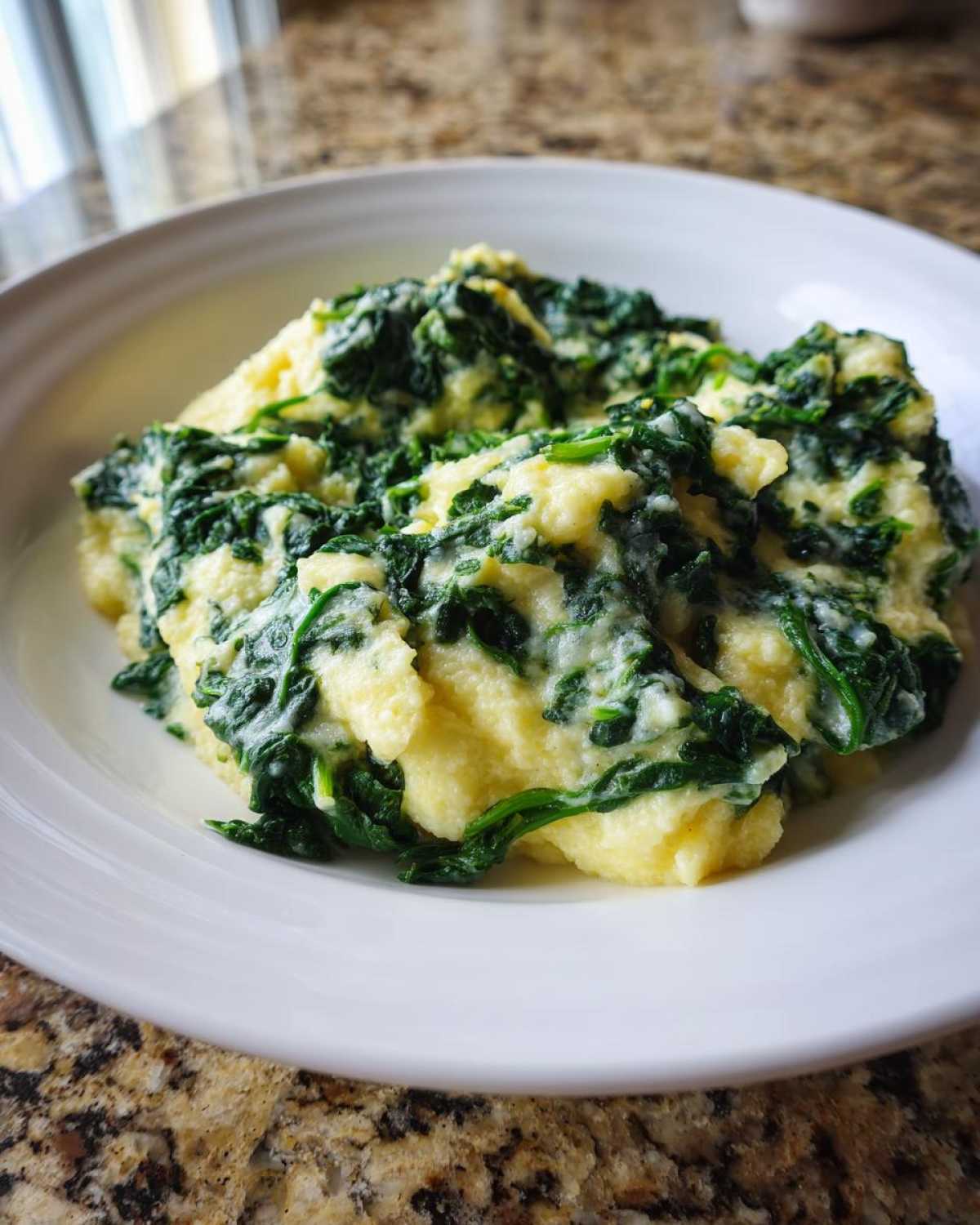 A close-up of a serving of One-Pot Creamy Spinach Parmesan Polenta in a white bowl.