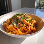 A close-up of One-Pot Creamy Tomato Basil Tortilla Pasta served in a white bowl, topped with fresh basil and grated cheese.