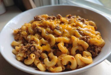 A close-up of a white bowl filled with creamy taco pasta mixed with seasoned ground beef and topped with melted cheddar cheese.