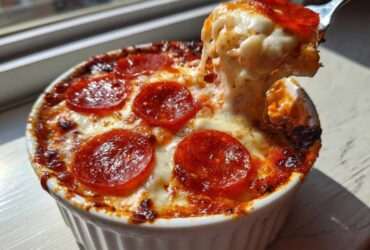 A fork pulls a cheesy, stringy bite from a baked cottage cheese pizza bowl topped with melted cheese and pepperoni.